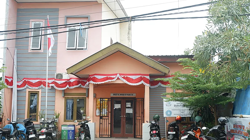 Bangunan Kantor Kelurahan Sudiang Makassar berwarna oranye dengan tiang bendera dan sepeda motor terparkir di depannya