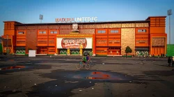 Fasad oranye Stadion Gelora Madura Ratu Pamelingan bertuliskan Madura United FC dengan baliho pemain, dua anak bersepeda di pelataran