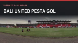 Lapangan dan tribune merah Stadion Kapten I Wayan Dipta di Gianyar pada siang hari dengan beberapa orang duduk di rumput, dengan teks judul "Bali United Pesta Gol" dan label Rubrik.co.id - Olahraga di bagian atas gambar