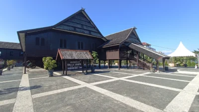 Bangunan kayu panggung bergaya rumah adat Bugis-Makassar bercat gelap dengan papan nama di depannya