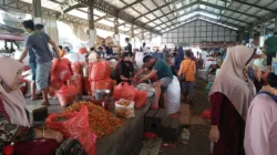 Pedagang dan pembeli di antara tumpukan karung cabai merah dan timbangan di dalam los pasar induk beratap baja