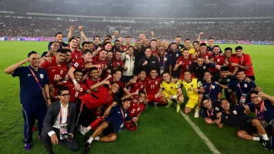 Skuad timnas Indonesia berkaus merah dan ofisial berfoto bersama di tengah lapangan stadion yang penuh penonton