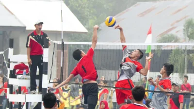 Dua pemain voli melompat berebut bola di atas net pada pertandingan lapangan terbuka yang ditonton warga