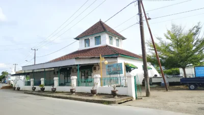 Masjid tua beratap tumpang dua tingkat berdinding putih dengan pagar besi hijau di tepi jalan