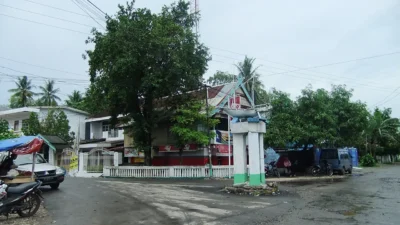 Persimpangan jalan di Bulukumba dengan tugu berbentuk perahu pinisi dan deretan rumah panggung di belakangnya