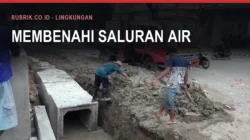 Dua pekerja menggali tanah di sisi jalan untuk memasang gorong-gorong beton berbentuk kotak, dengan truk dan deretan kios di latar belakang, serta teks judul "Membenahi Saluran Air" dan label Rubrik.co.id - Lingkungan di bagian atas gambar
